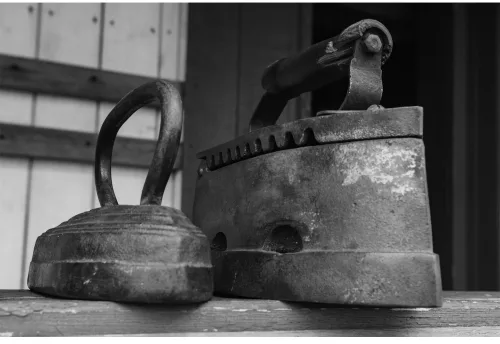 Black and white photograph of three vintage cast iron cooking vessels arranged on a wooden surface with industrial background.