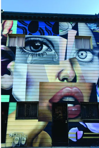 A stylised fragmented face composed of geometric sections in blue, pink, cream and black tones, reminiscent of urban street art.