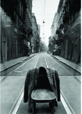 Black and white photograph of a pram standing alone on tram tracks running down the centre of a symmetrical European street lined with tall buildings.