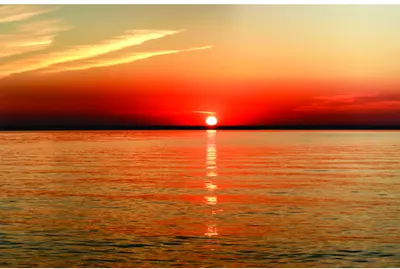 A photographic image of a large sun on the horizon reflecting onto calm water at sunset, with golden and orange tones dominating the sky.