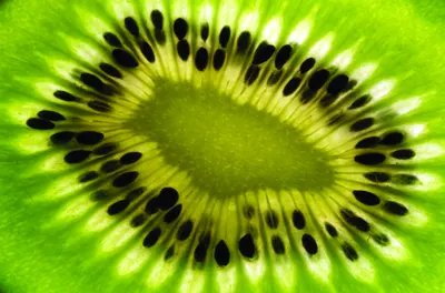 A photograph of a kiwi fruit sliced in half, showing the bright lime-green flesh and small black seeds arranged in a radial pattern.