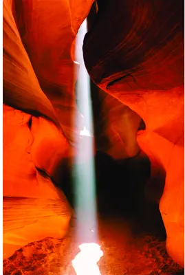 A photograph of narrow slot canyon walls in deep orange and red tones with a bright beam of light streaming down through the centre.
