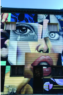 A stylised fragmented face composed of geometric sections in blue, pink, cream and black tones, reminiscent of urban street art.