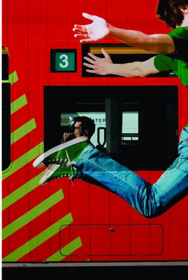 Collage artwork of a person in casual clothes climbing a bright red wall marked with green diagonal stripes, surrounded by fragmented urban imagery.