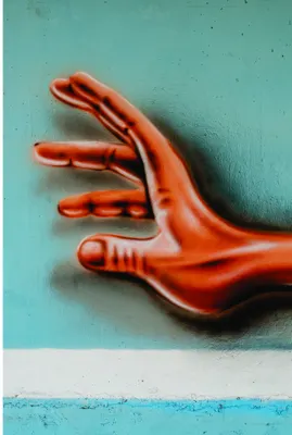 A bright red ceramic hand sculpture reaches outward against a distressed turquoise painted wall.