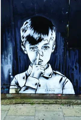 A black and white street art mural of a young boy with a contemplative expression, resting his chin on his hand.