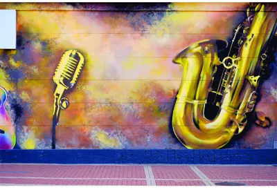 Street art mural showing a golden vintage microphone on the left and a golden saxophone on the right against a textured background of warm yellows, oranges and cool purples and blues.