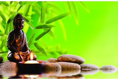 A bronze Buddha statue sits on river stones beside a lit candle, framed by bright green bamboo leaves against a luminous yellow-green background.