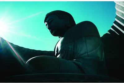 A black silhouette of a man sitting in a meditative pose against a bright turquoise and cream sky.